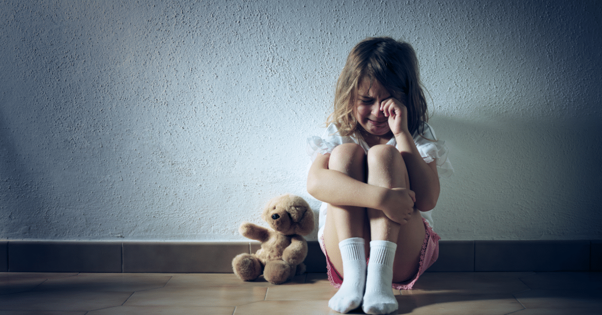 Little girl struggling with her mental health, sat on the floor crying with a teddy