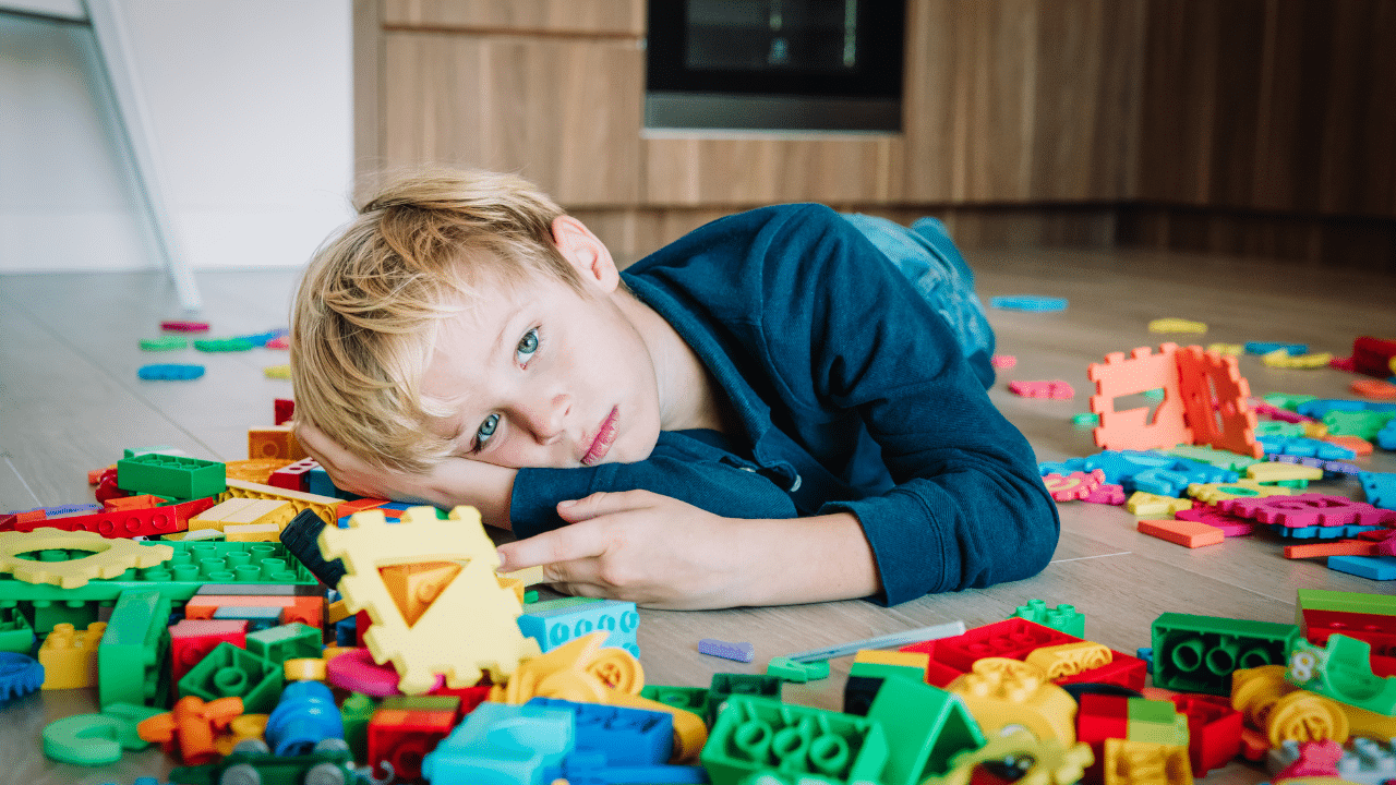 Young boy laying on the floor amongst toys looking sad